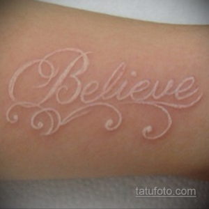 Фотография белой татуировки с надписью "Believe" (верь) на коже. Рисунок выполнен каллиграфическим шрифтом и украшен завитушками.