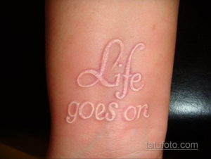 Фото белой татуировки с надписью 'Life goes on' на руке. Мотивирующий и вдохновляющий рисунок, выполненный каллиграфическим шрифтом.