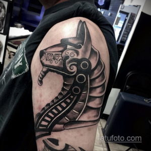 Фото тату драккара на плече мужчины в стиле blackwork. Детализированный рисунок корабля викингов с резными элементами и кругами.