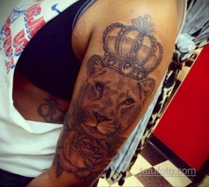 Фото татуировки на плече: львица в короне, окруженная розами, выполненная в реалистичном стиле с использованием ярких цветов.