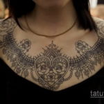 Фото тату на груди и плечах, имитирующее кружево с розами и сердечком. Детализированный рисунок татуировки.