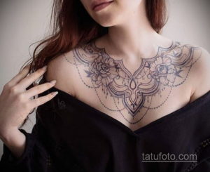 Фото тату в стиле line work, изображающее цветы и геометрические узоры, расположенное на груди и плечах женщины.