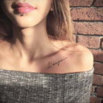 Фото тату: небольшая татуировка надписью 'L'espoir' на ключице девушки, выполненная черными чернилами в каллиграфическом стиле.