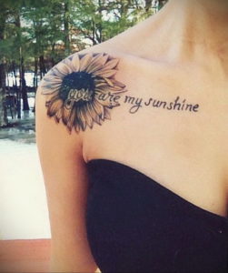 Фото тату: реалистичный подсолнух с надписью "You are my sunshine" на плече. Детализированный рисунок татуировки с яркими и теплыми оттенками.