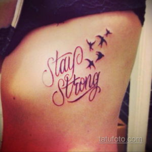 Фото тату: надпись "Stay Strong" в каллиграфическом стиле с изображением летящих птиц, расположенная на боку. Символ надежды и силы.