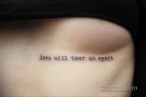 Фото тату: черная надпись 'love will tear us apart' на боку, выполненная тонкой линией. Минималистичный рисунок татуировки для девушек.