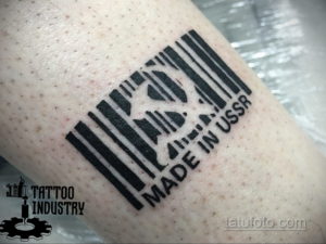Фото тату на руке в виде штрихкода, внутри которого просматривается силуэт медведя и надпись 'MADE IN USSR'. Черно-белый рисунок татуировки.