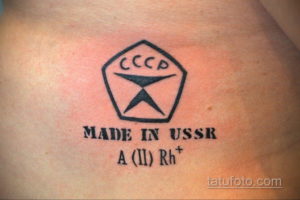 Фото тату на плече с изображением советского знака качества и надписью 'MADE IN USSR'. Черно-белый рисунок татуировки в минималистичном стиле.