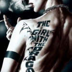 Фото тату на спине мужчины с цитатой "The Girl With The Dragon Tattoo" и изображением дракона. Черно-белая татуировка в готическом стиле.