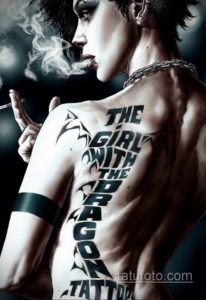 Фото тату на спине мужчины с цитатой "The Girl With The Dragon Tattoo" и изображением дракона. Черно-белая татуировка в готическом стиле.