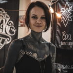 Фотография девушки с татуировками в стиле геометрии на шее и ключице. Четкие линии и узоры создают эффект украшения.