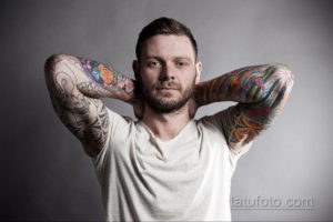 Фотография мужчины с яркими татуировками в стиле традиционной японской татуировки на руках. Изображены цветы, волны и другие элементы японской культуры.