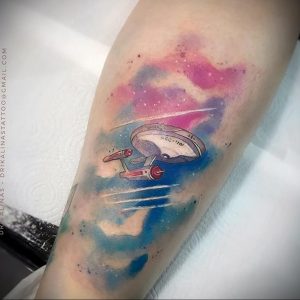 Фото акварельной татуировки космического корабля на руке. Нежные пастельные тона, размытые линии, создает эффект невесомости.