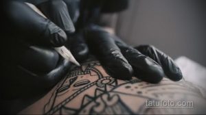 Фото тату процесса нанесения черного рисунка на руку. Крупный план руки мастера в черных перчатках и тату-машинки.
