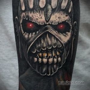 Фото тату Эдди от Iron Maiden на руке, выполненное в реалистичном стиле с использованием черных, серых и красных оттенков. Детализированный рисунок татуировки.