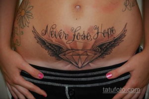 Фото татуировки в виде бриллианта с расправленными крыльями и надписью 'Never Lose Hope' на женском животе. Вдохновляющий и красивый рисунок татуировки.