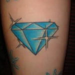 Фото тату голубого бриллианта на ноге. Рисунок татуировки с добавлением блесток и звезд. Эскиз тату для девушек, любящих яркие и необычные украшения.
