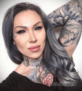 Фотография девушки с ярким макияжем и татуировками на шее и руке. Девушка смотрит в камеру, демонстрируя свою уверенность и стиль.