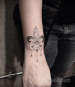 Фото минималистичной татуировки флёр-де-лис на запястье. Тонкие линии и точечные элементы создают элегантный и сдержанный образ.