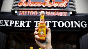 Фотография фасада тату-студии Daredevil Tattoo Museum с вывеской и рукой, держащей бутылку острого соуса Cholula.