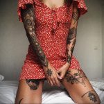 Фото татуировок на руках и ногах девушки в красном платье. Татуировки включают в себя геометрические узоры, цветы и черепа, выполненные в черном цвете.