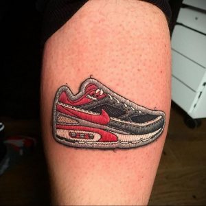 Фото тату: реалистичная татуировка кроссовок Nike Air Max на икре. Изображение выполнено в ярких цветах, с детальной проработкой текстур.