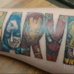 Цветная татуировка на руке с изображением логотипа Marvel, буквы которого заполнены портретами различных супергероев.