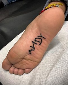 Фото тату на стопе: надпись "ANDY", выполненная черными чернилами в простом и лаконичном стиле.