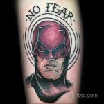 Фото тату Карателя на руке с надписью "No Fear" в круге. Изображение выполнено в реалистичном стиле с использованием красных, черных и серых оттенков.