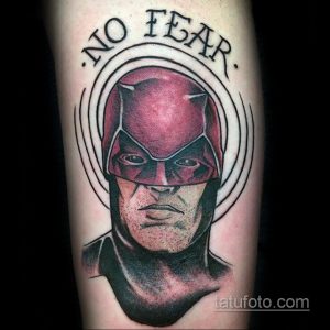 Фото тату Карателя на руке с надписью "No Fear" в круге. Изображение выполнено в реалистичном стиле с использованием красных, черных и серых оттенков.