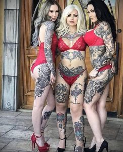 Фото трех девушек с татуировками на теле, одетых в красное белье. Изображение демонстрирует женственный стиль и красоту татуировок.