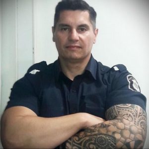 Фотография полицейского в форме с детализированной татуировкой на предплечье, демонстрирующая силу и профессионализм.