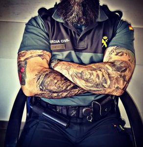 Фотография сотрудника Guardia Civil с масштабной татуировкой на обеих руках. Рисунок татуировки изображает портрет мужчины в старинном стиле.