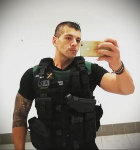 Фотография полицейского в тактическом жилете и с татуировками на руке. Он делает селфи, демонстрируя свою готовность к выполнению долга.
