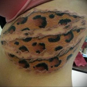 Фото татуировки, имитирующей леопардовую шкуру на бедре. Реалистичный рисунок с эффектом разорванной кожи.