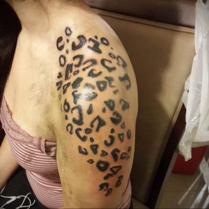 Фото тату минималистичного леопардового принта на плече. Черные пятна разной формы, простой дизайн, стильный вид.