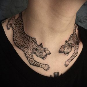 Черно-белое фото татуировки на шее и ключицах с изображением двух бегущих леопардов, выполненной в минималистичном стиле.