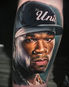 Фото тату на руке: реалистичный портрет рэпера 50 Cent в бейсболке. Высокодетализированная татуировка с точной передачей черт лица и текстуры кожи.