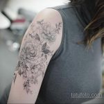 Фотография женского плеча, украшенного изящной татуировкой с изображением букета цветов в стиле ботанической иллюстрации.