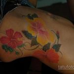 Фото тату с изображением ярких цветов гибискуса на боку. Красные, желтые и оранжевые оттенки создают тропическую атмосферу.