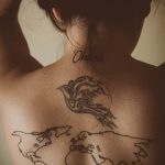 Фото тату: татуировка на спине с изображением карты мира и надписи "Ohana". Детализированный рисунок в стиле графика.