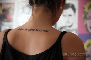 Фото тату с надписью 'follow the yellow brick road' на затылке девушки. Простой, элегантный дизайн, выполненный черным цветом.