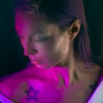 Фото минималистичной татуировки в виде маленькой черной звезды на шее девушки.