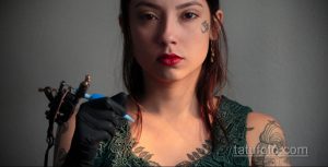 Фото: мастер тату делает татуировку девушке. Видна тату-машинка, рука мастера в перчатке и часть готовой татуировки на плече.