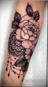 Фото тату на предплечье, сочетающее в себе цветы и мандалу в стиле blackwork. Детализированный рисунок татуировки с геометрическими узорами.