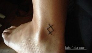 Фото тату с изображением руны на лодыжке. Татуировка выполнена в черном цвете и имеет геометрическую форму.