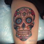 Фото тату: красочный сахарный череп (Calavera) на бедре, выполненный в традиционном мексиканском стиле с яркими цветами и узорами.