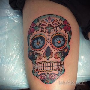 Фото тату: красочный сахарный череп (Calavera) на бедре, выполненный в традиционном мексиканском стиле с яркими цветами и узорами.