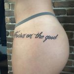 Фото тату на боку девушки: черная надпись "Focus on the good" выполненная красивым каллиграфическим шрифтом. Минималистичная татуировка с позитивным посылом.