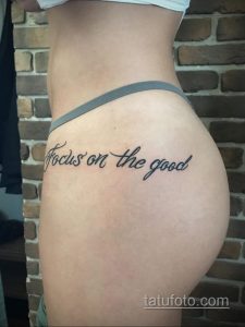 Фото тату на боку девушки: черная надпись "Focus on the good" выполненная красивым каллиграфическим шрифтом. Минималистичная татуировка с позитивным посылом.